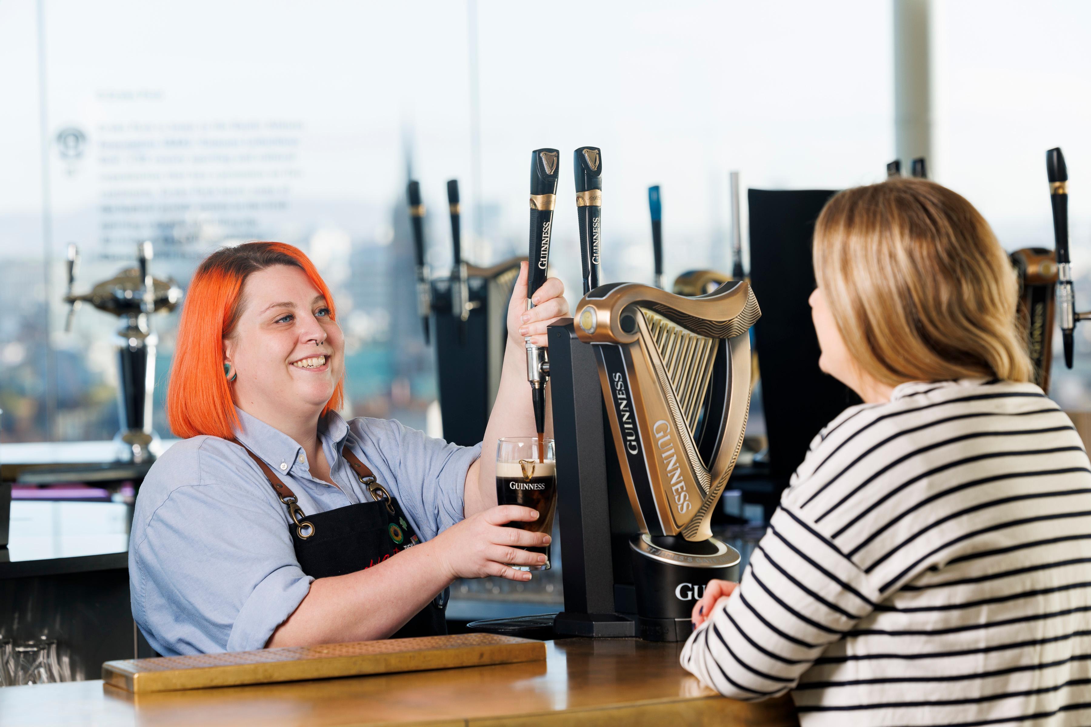 Woman with orange hair pouring a pint of Guiness behind a bar
