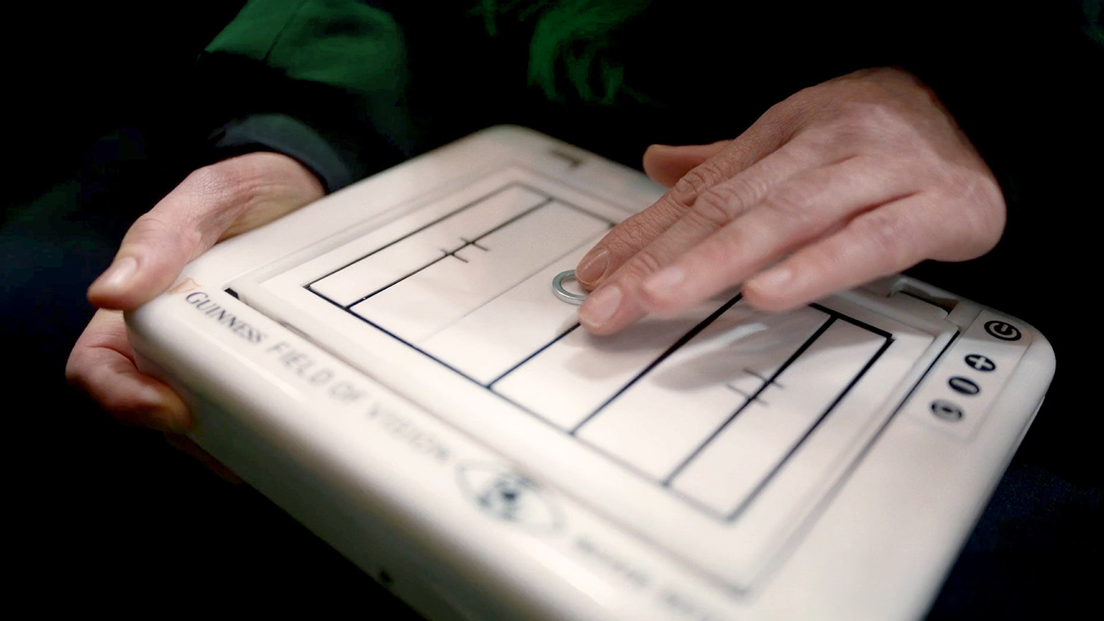 A close-up of a person’s hands using a tactile Field of Vision tablet that displays a raised outline of a rugby pitch, allowing them to feel the layout through touch.